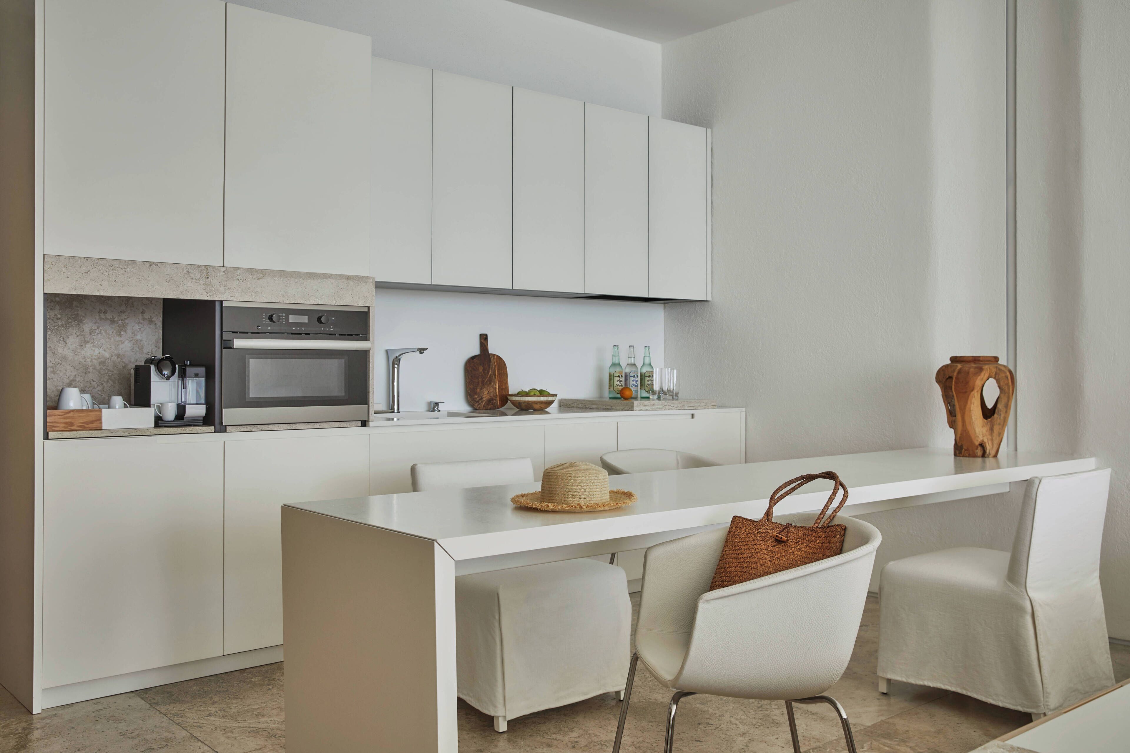 A modern kitchen with white cabinetry, a built-in oven, and a dining area with two chairs and a small table.