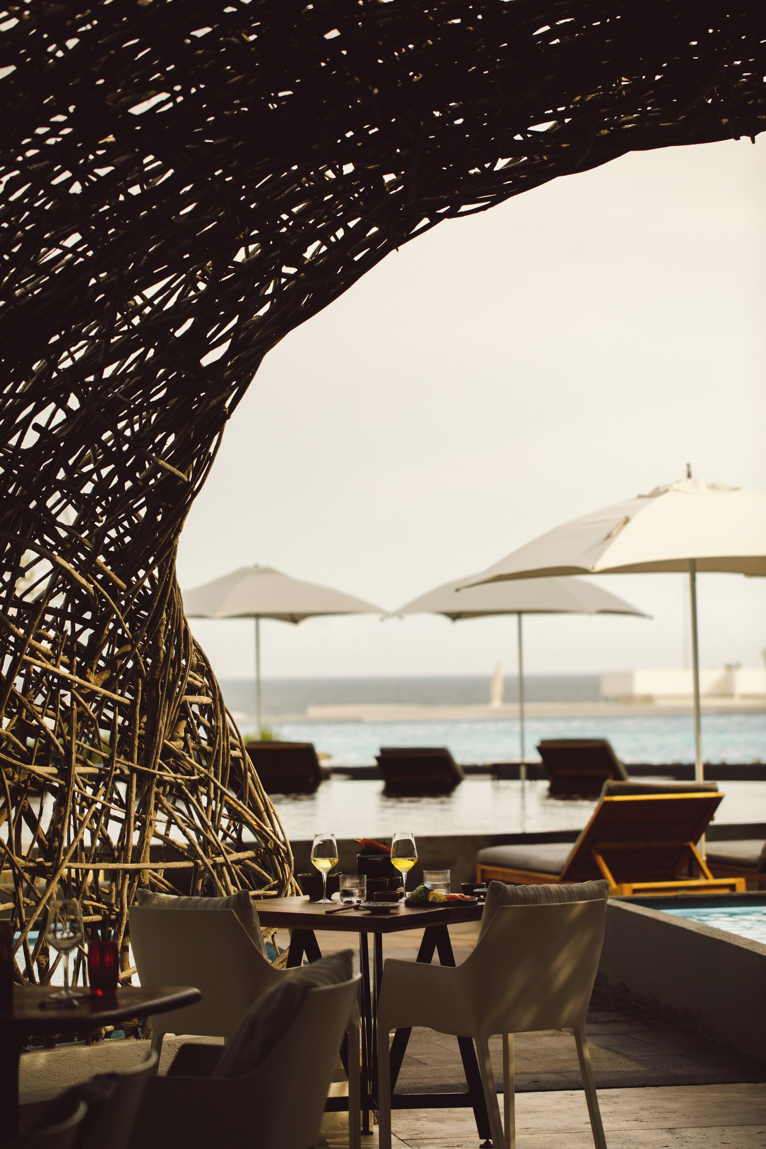 A poolside area with wicker furniture, umbrellas, and lounge chairs.