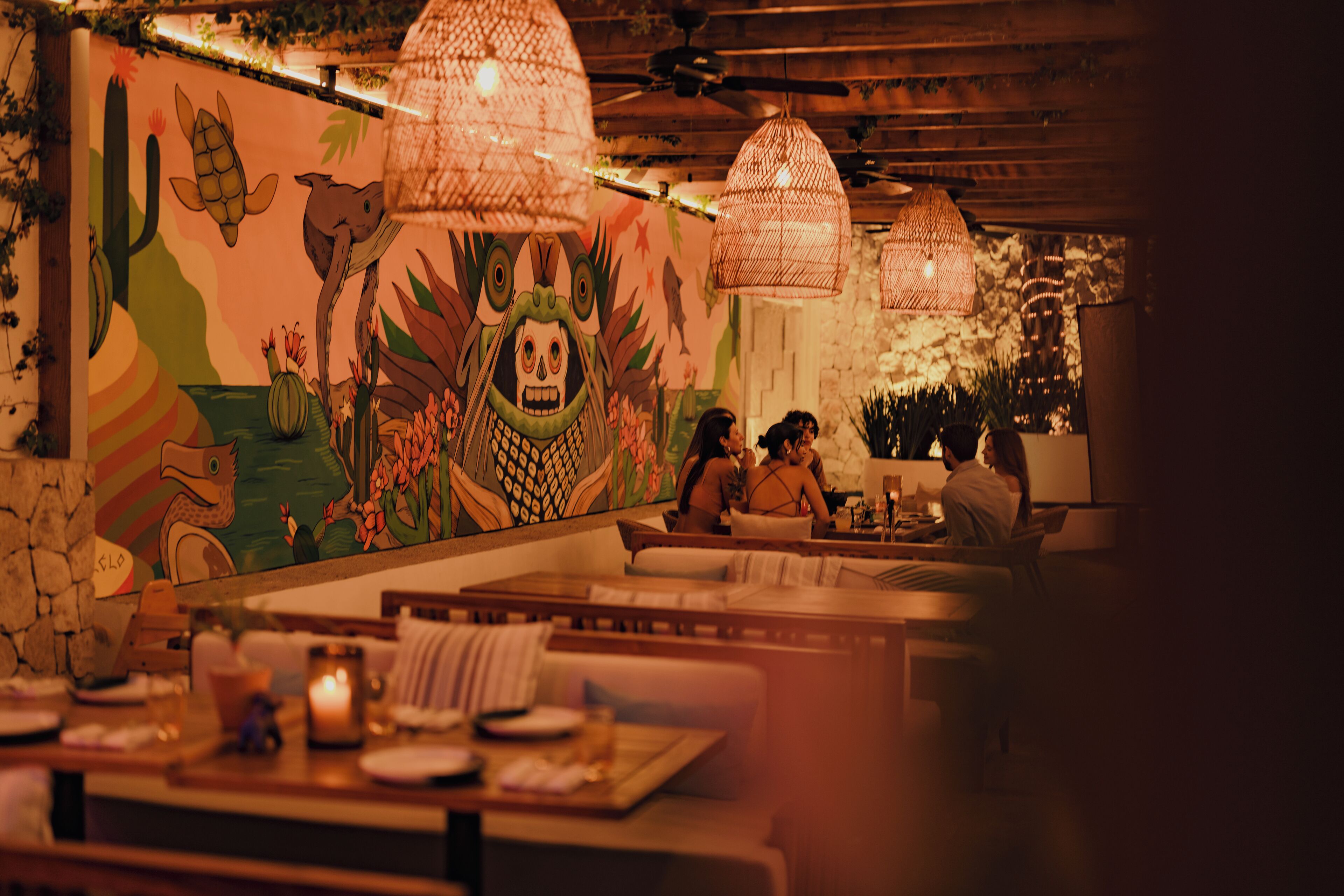 A restaurant with a mural, wicker pendant lights, and a stone wall.