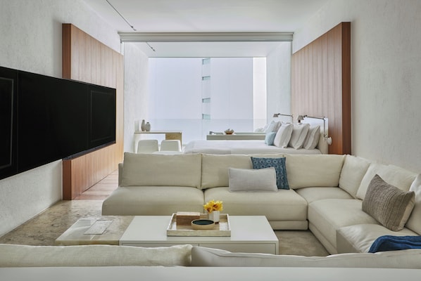 Una sala de estar moderna con un televisor de pantalla plana grande, un sofá seccional color beige, una mesa de centro con adornos y vistas a un balcón con barandilla y ventana.