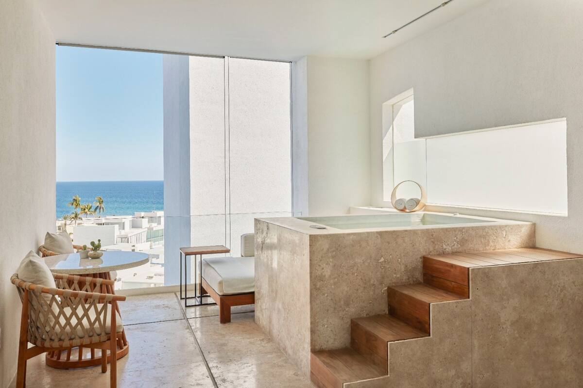 Un baño moderno con una bañera grande, una escalera de madera y vista al océano.