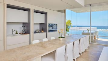 Una cocina moderna con una larga mesa de comedor, sillas blancas y vistas al océano.