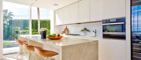 A modern kitchen with a large island, bar stools, and a view of greenery outside.