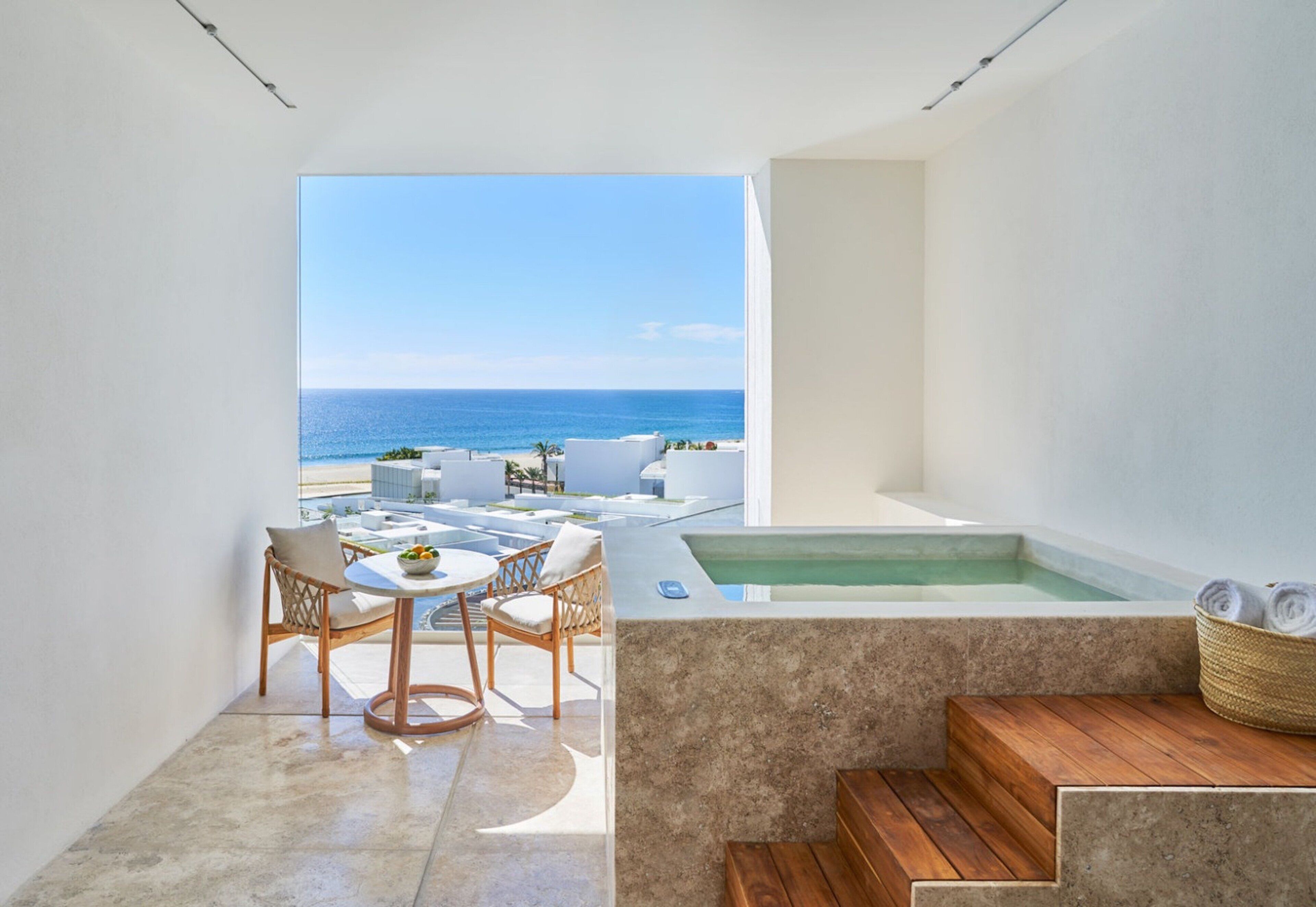 Un área de estar moderna al aire libre con vista al mar, una bañera de hidromasaje y un banco de madera.
