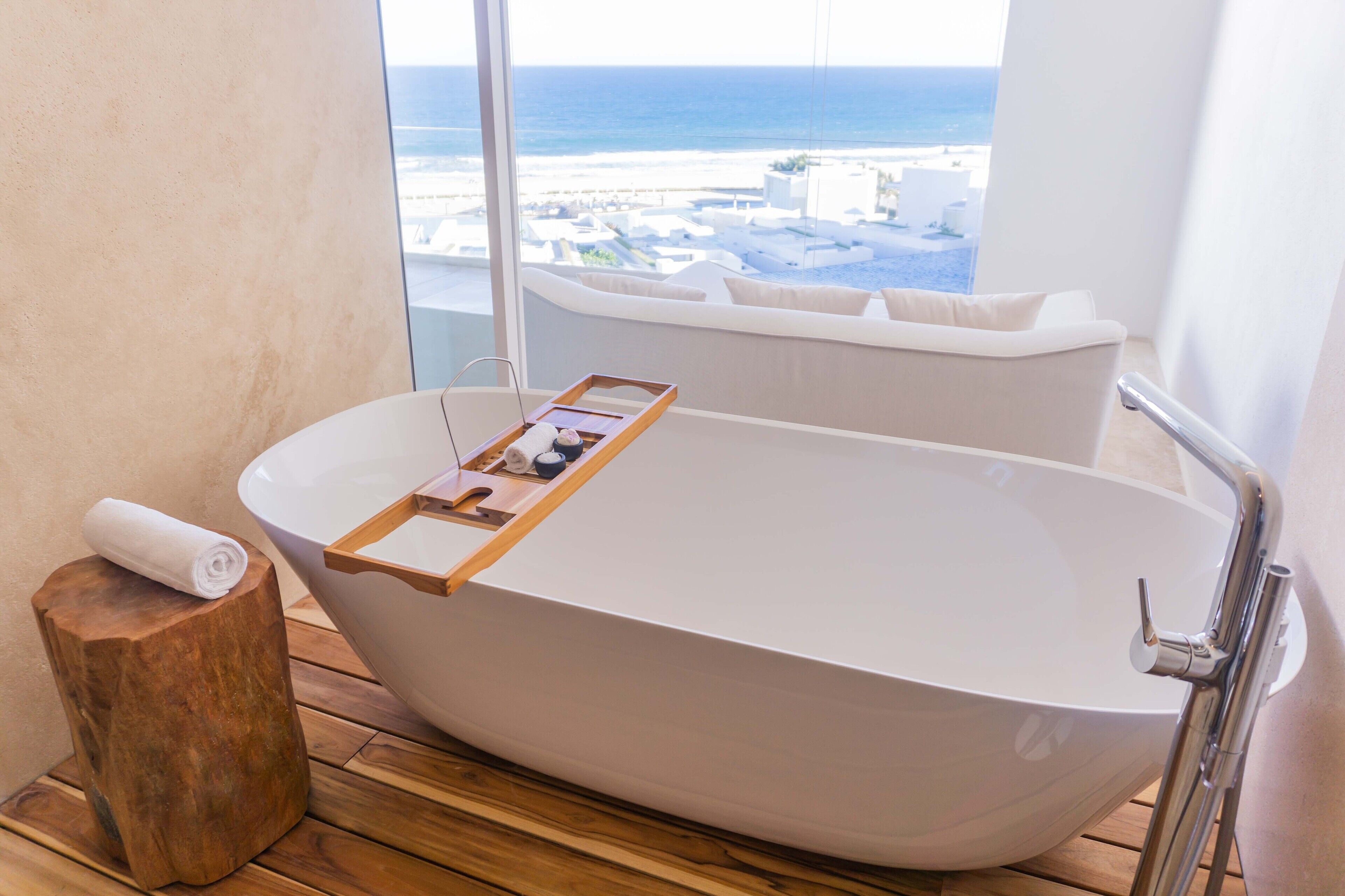 A modern bathroom with a freestanding bathtub, wooden side table, and a towel on a wooden stool.