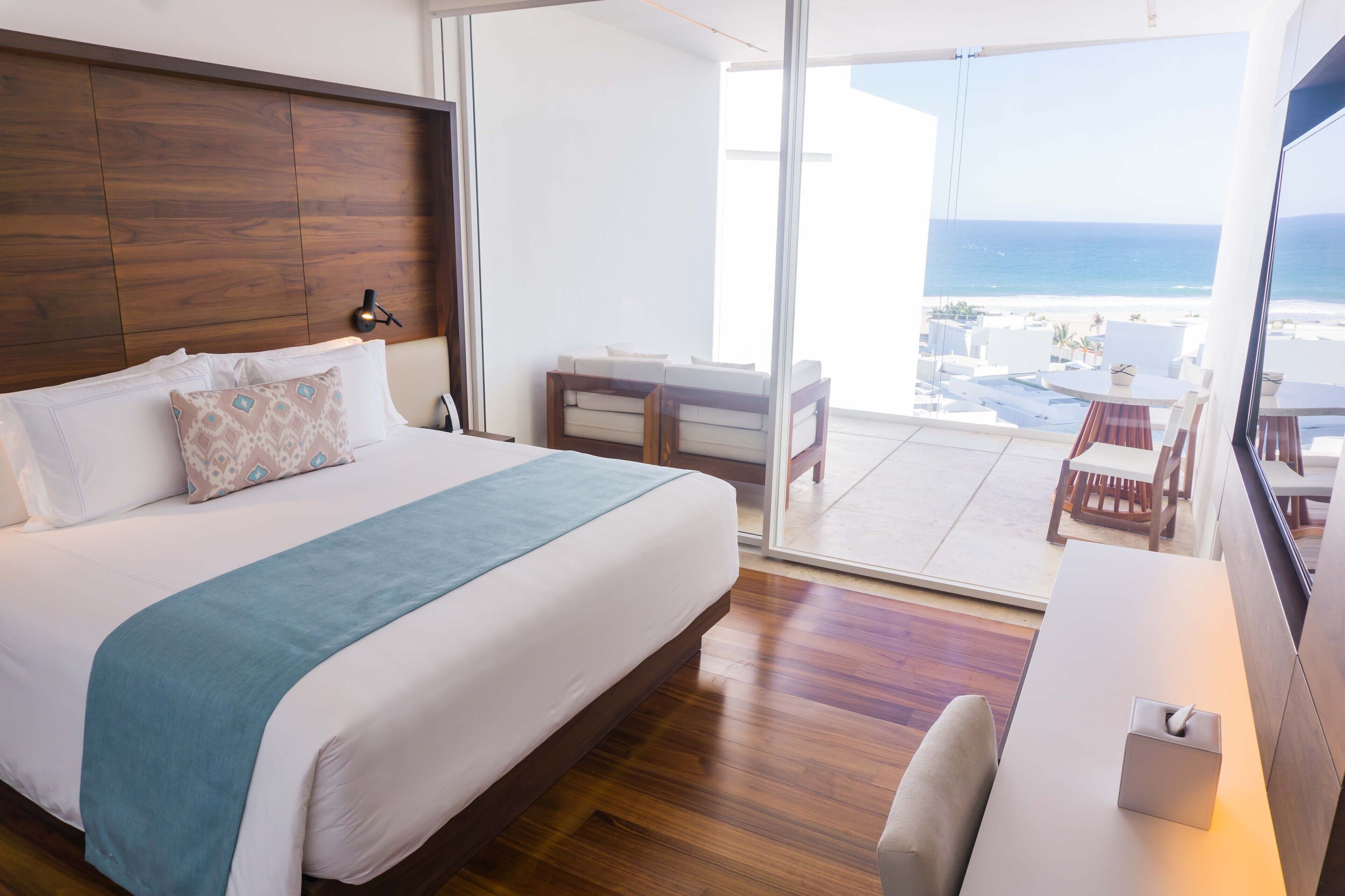 Ein Hotelzimmer mit einem großen Bett, einem Schreibtisch und einem Balkon mit Meerblick.
