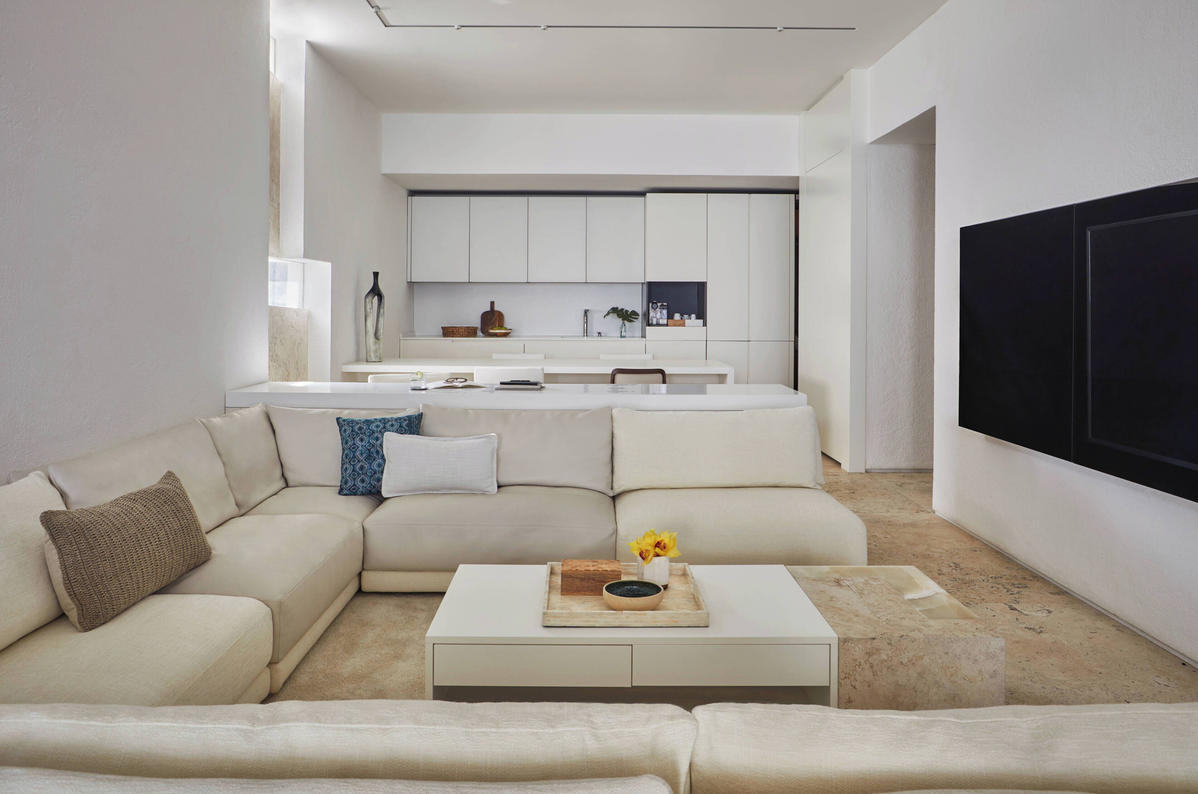 A modern living room with a large sectional sofa, a coffee table with decorative items, and a kitchen in the background.
