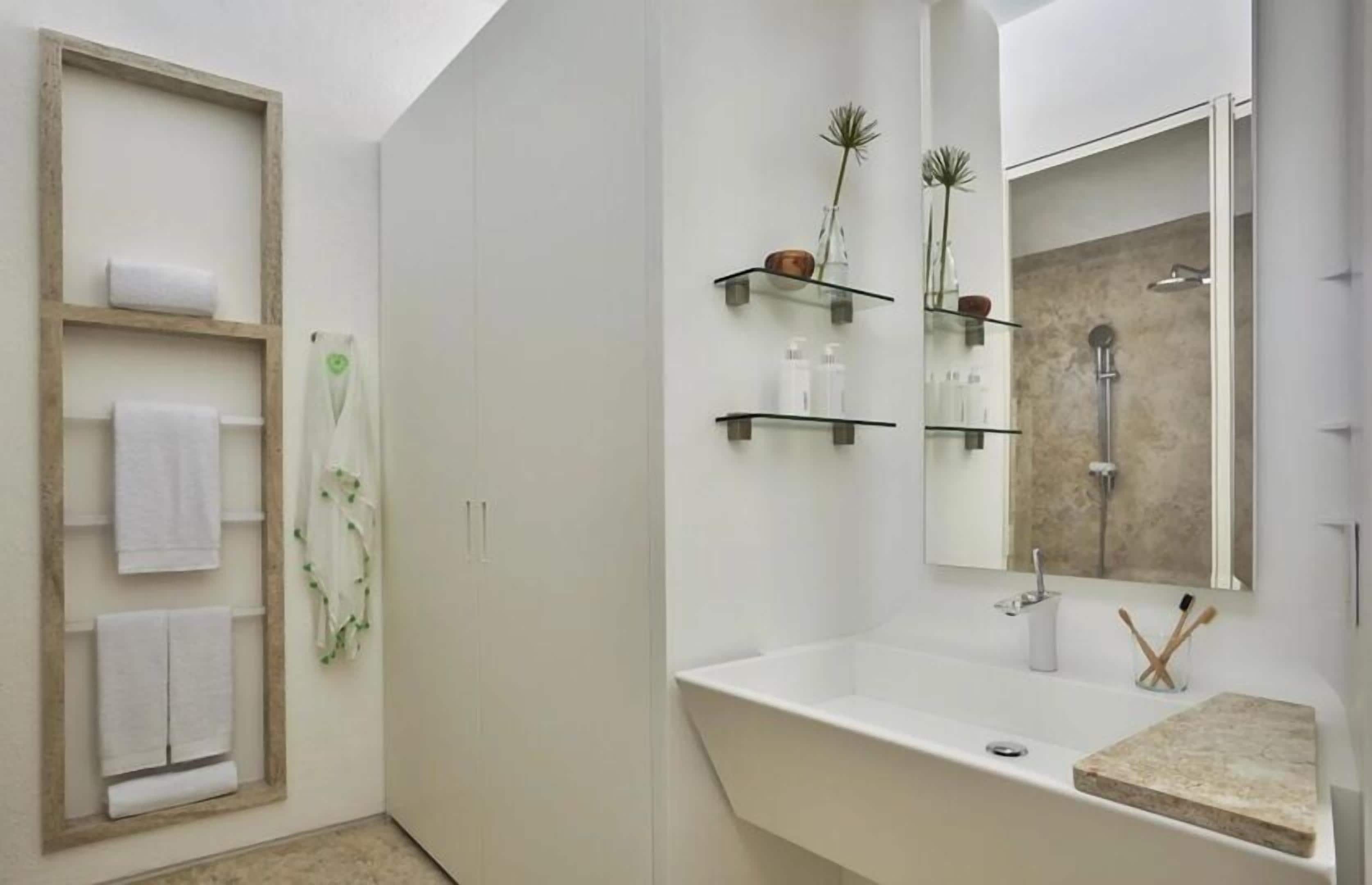A modern bathroom with a large mirror, a sink, and a shower. There are shelves with toiletries and towels.