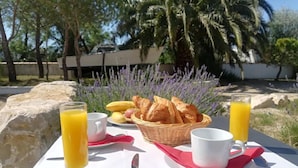 A breakfast setup with croissants, fruit, and orange juice on a table outdoors. - Hôtel Clamador (Saintes-Maries-de-la-Mer)