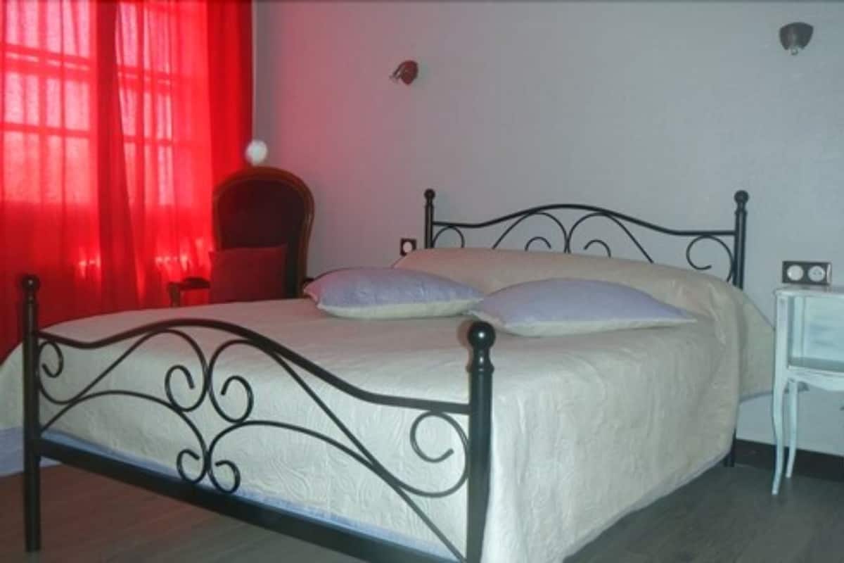 Een enkel bed met een metalen frame en witte beddengoed in een kamer met een rood gordijn en een klein nachtkastje.