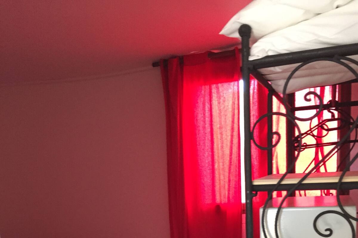 Een kleine kamer met een stapelbed, een enkel bed, een rood gordijn en een betegelde vloer.