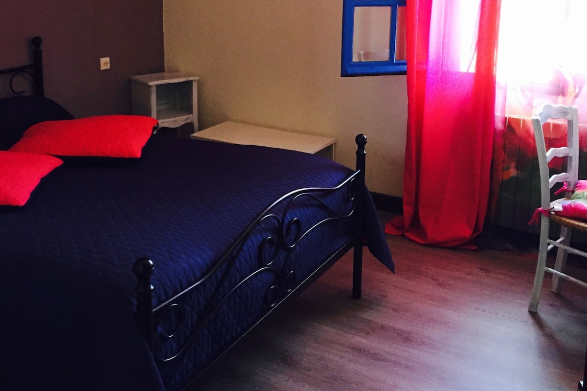 Een slaapkamer met een bed, een stoel, een klein tafeltje en een raam met gordijnen.