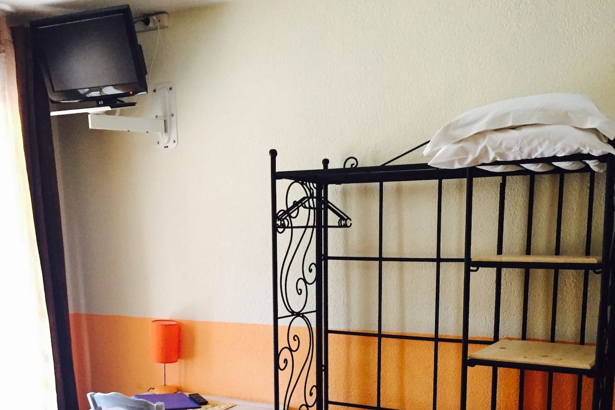 Een studentenkamer met een stapelbed, een bureau, een stoel, een aan de muur bevestigde televisie en een plank.