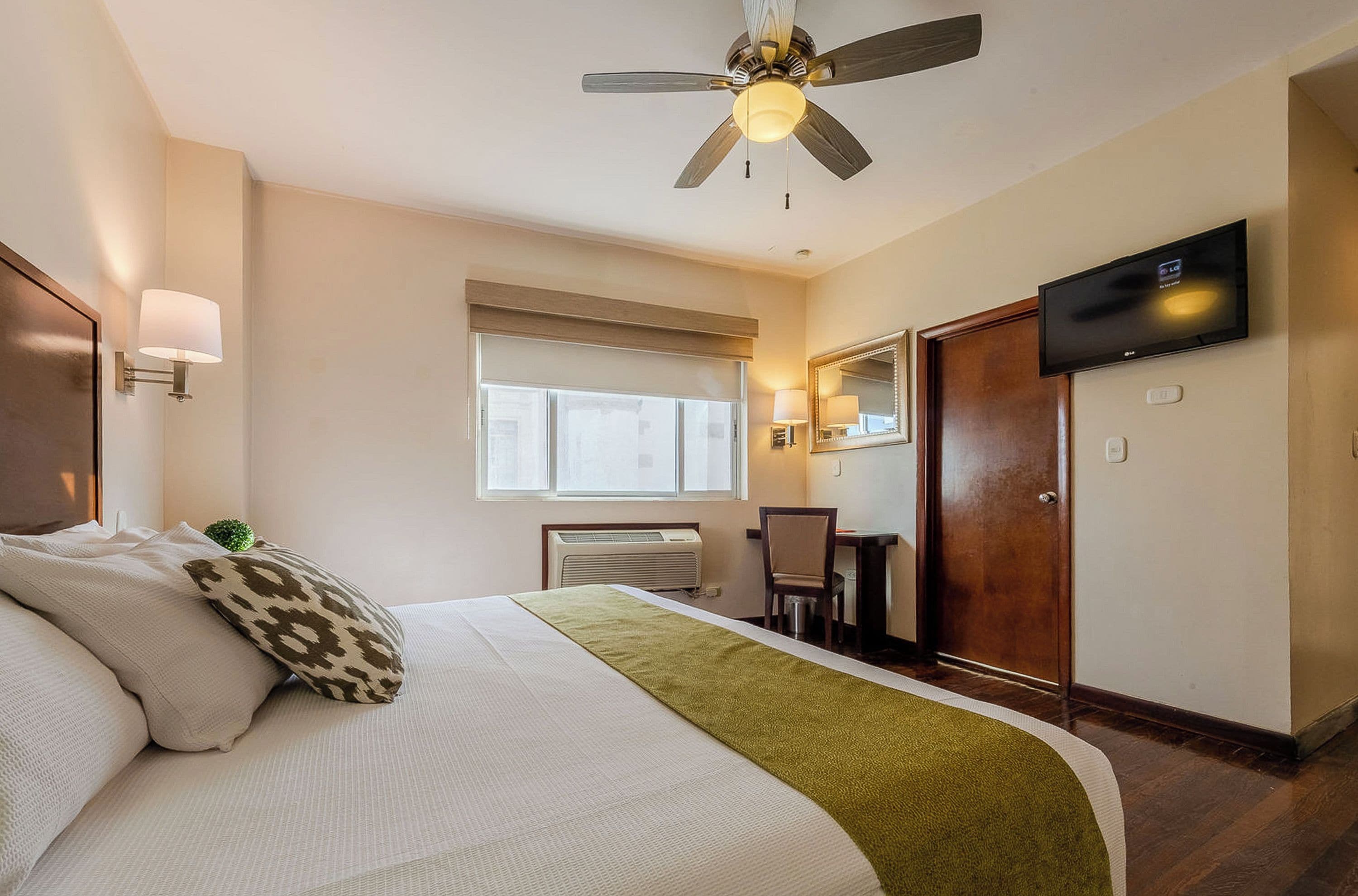 Une chambre d’hôtel avec un lit, un ventilateur de plafond, une télévision, une fenêtre et une porte.