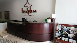 A hotel reception desk with a wooden counter, a sign above it, and a bulletin board with various items. - Hotel Plaza Chihuahua (Chihuahua)