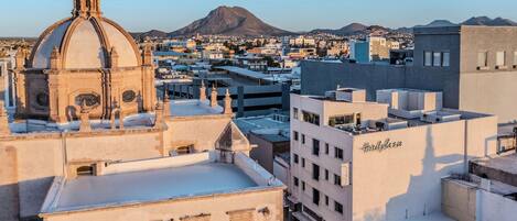 A cityscape with a prominent church dome, a modern building labeled 'Hotel Plaza,' and a mountain in the background.