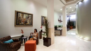 Un vestíbulo moderno con un cuadro grande, un mostrador de recepción y una zona de estar con sofá y reposapiés.
