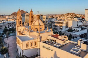 Una plaza hotelera con un edificio grande que presenta una cúpula y dos torres, rodeada de otros edificios y un paisaje montañoso al fondo.
