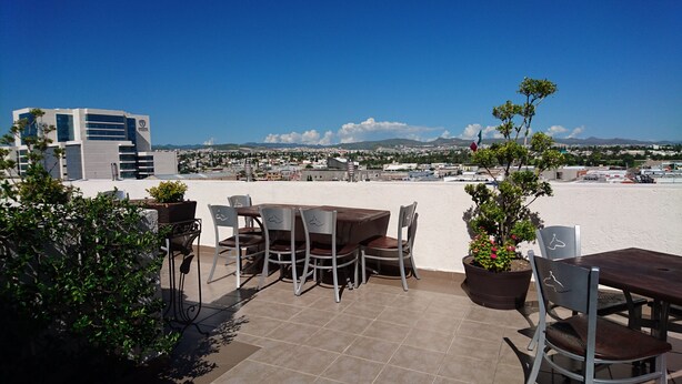 Un patio al aire libre con una mesa y sillas, plantas en macetas y vistas a un paisaje urbano y montañas a lo lejos.