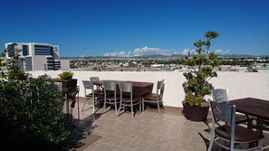 An outdoor patio with a table and chairs, potted plants, and a view of a cityscape and mountains in the distance. - Hotel Plaza Chihuahua (Chihuahua)