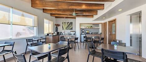 A modern dining area with wooden beams, black chairs, and a central island with a coffee machine.