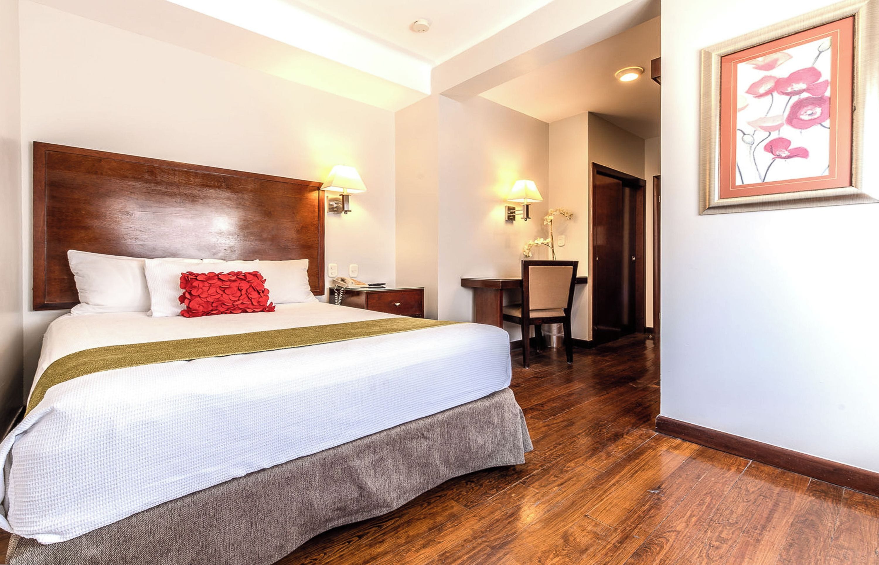 Una habitación de hotel con una cama grande, un cabecero de madera, un escritorio con una silla y una obra de arte enmarcada en la pared.