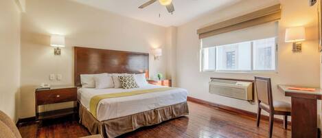 A hotel room with a bed, bedside table, lamp, desk, chair, and a ceiling fan.