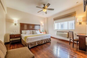 Habitación de hotel con cama, mesita de noche, lámpara, escritorio, silla y ventilador de techo.