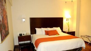 Una habitación de hotel con una cama grande, una mesita de noche, una silla y un cuadro en la pared.