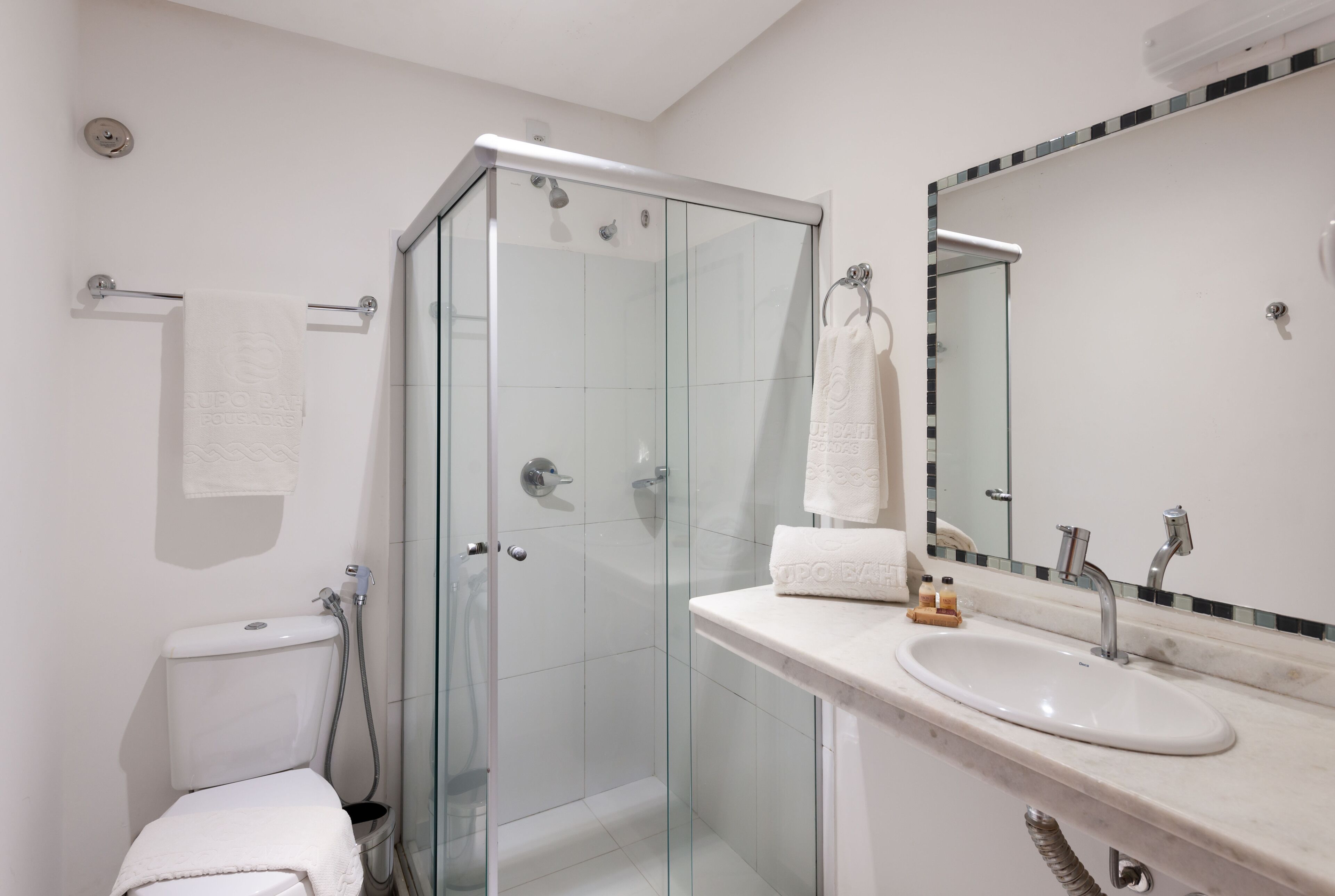 A modern bathroom with a glass-enclosed shower, a white sink, and a mirror with a black and white tile border.