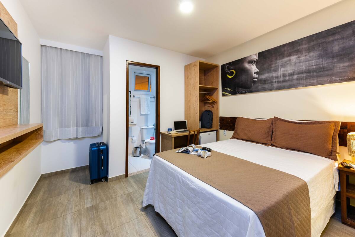 A hotel room with a bed, bedside table, lamp, and a large painting on the wall.
