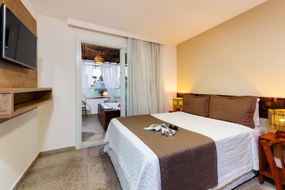 Habitación de hotel con una cama grande, un televisor montado en la pared, un escritorio con una silla y vistas a través de una puerta.