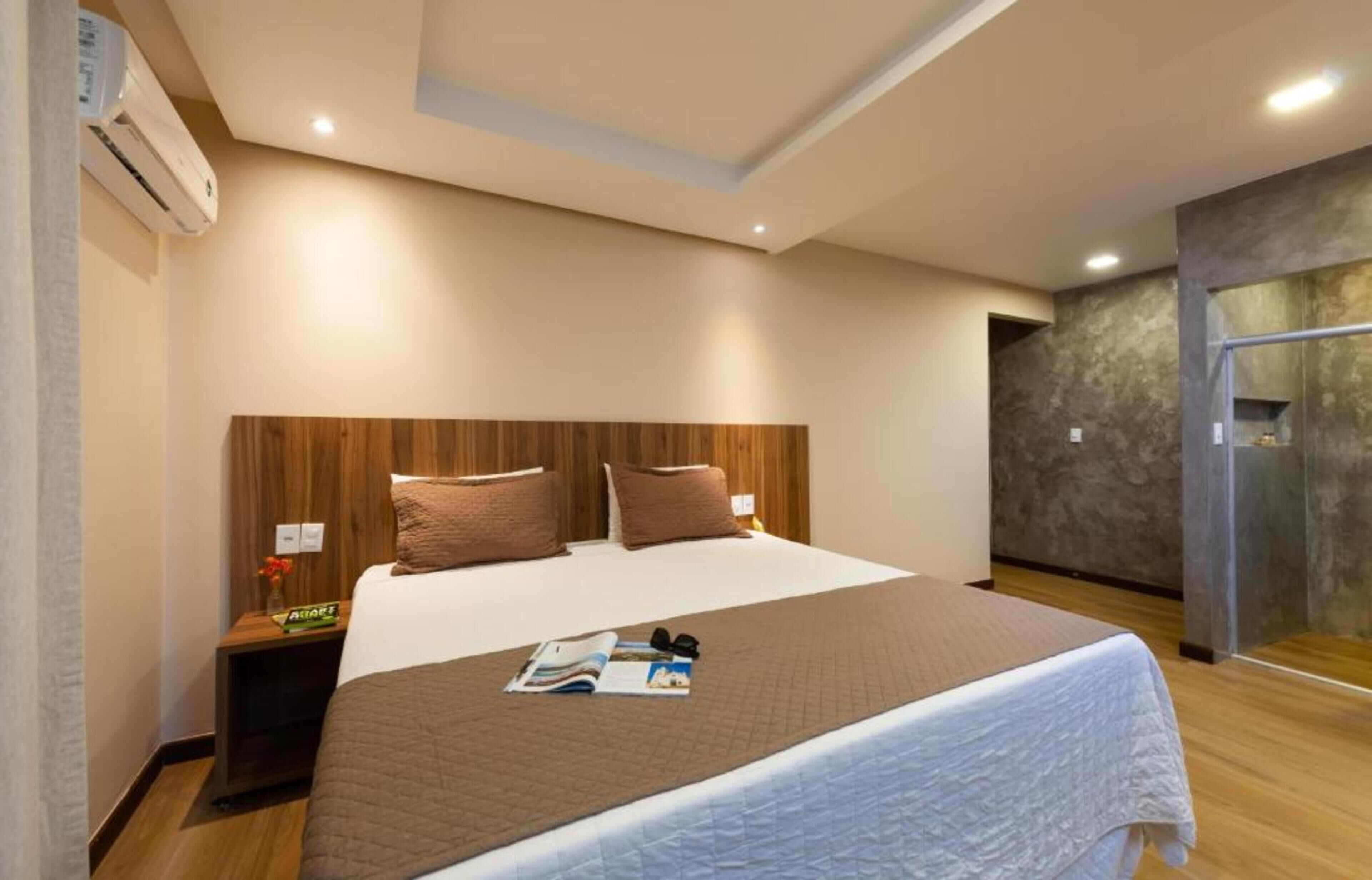 A hotel room with a large bed, wooden headboard, and a nightstand with a lamp.