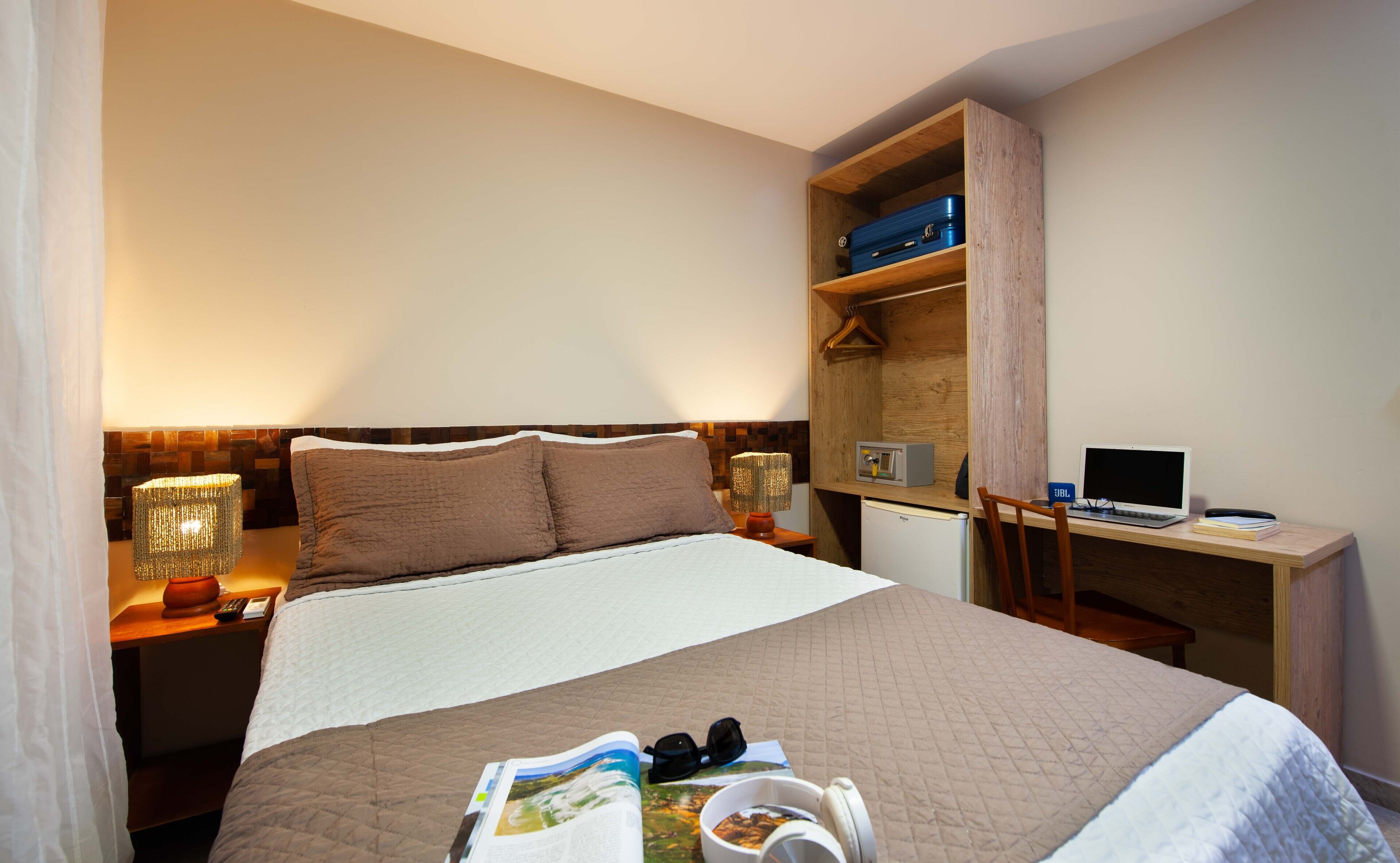 A hotel room with a bed, bedside lamps, a desk with a laptop, and a bookshelf.