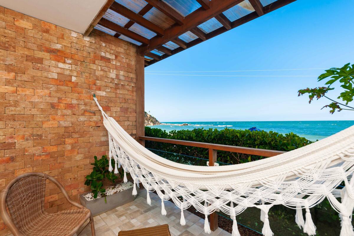 A hammock on a balcony with a view of the ocean.