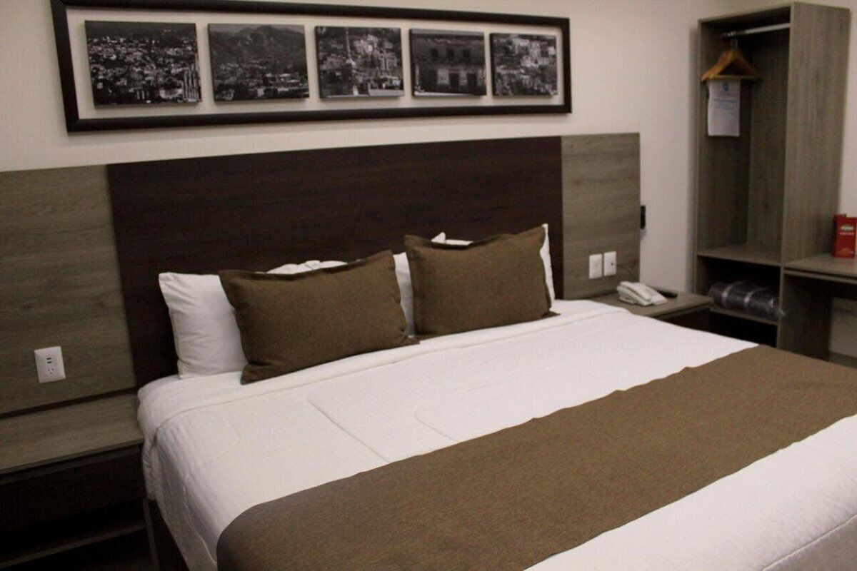 Habitación de hotel con una cama grande, cabecera de madera, mesita de noche, armario y una foto enmarco sobre la cama.