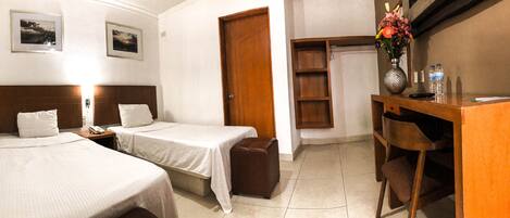 A hotel room with two single beds, a wooden desk with a vase of flowers, a chair, and a small cabinet.