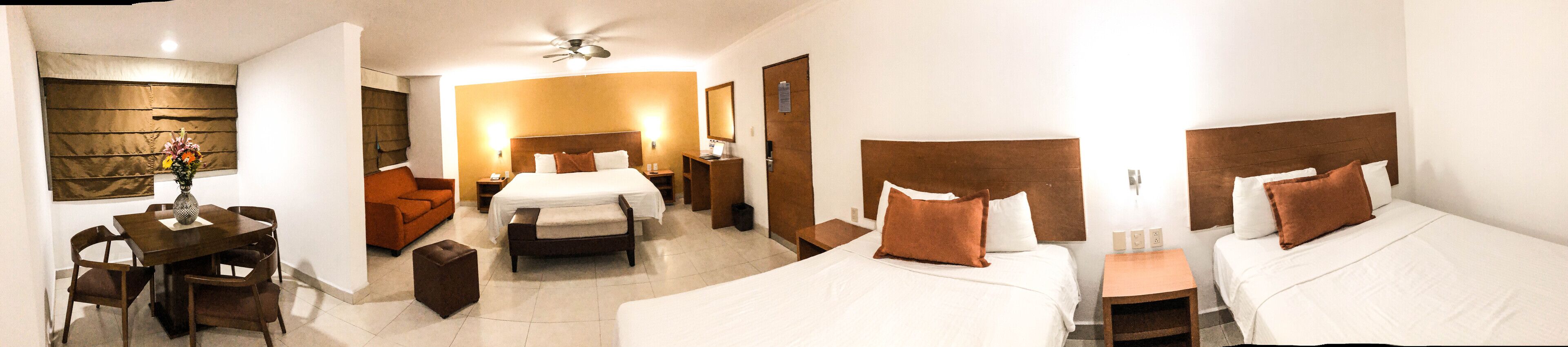 A hotel room with a large bed, a smaller bed, a sofa, a dining table, and a ceiling fan.