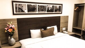 A hotel room with a large bed, a nightstand with a vase of flowers, a framed photo collage on the wall, and a wardrobe with a hanging rack. - Hotel River Poliforum (León)
