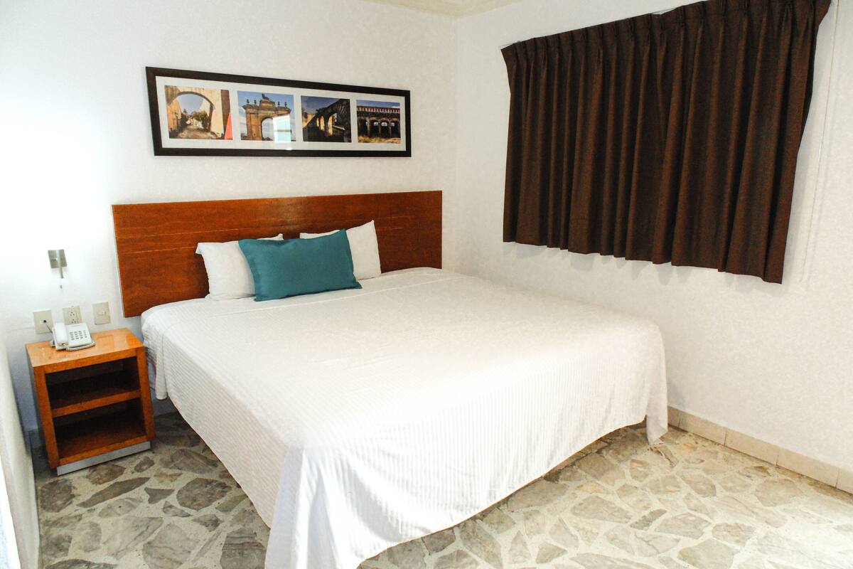 A hotel room with a bed, a nightstand with a phone, and a stone floor.