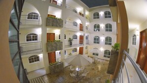 A multi-level atrium with a central open area featuring a table and chairs, surrounded by balconies and windows. - Hotel River Poliforum (León)