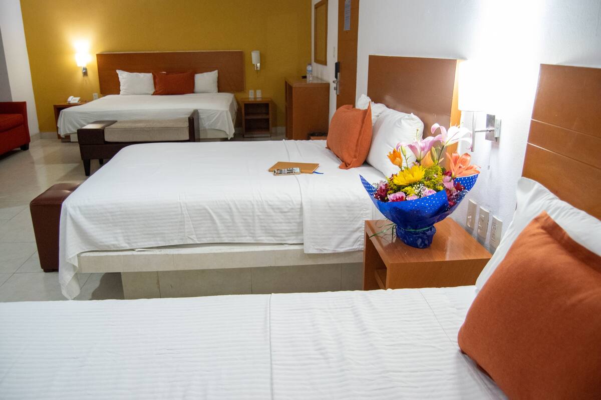 A hotel room with two beds, a bedside table with a vase of flowers, and a red chair.