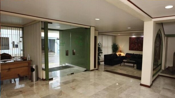 Un hall d’entrée spacieux avec un sol en marbre, un comptoir de réception, un coin salon avec un canapé et des fauteuils, et un mur d’accent de couleur verte.