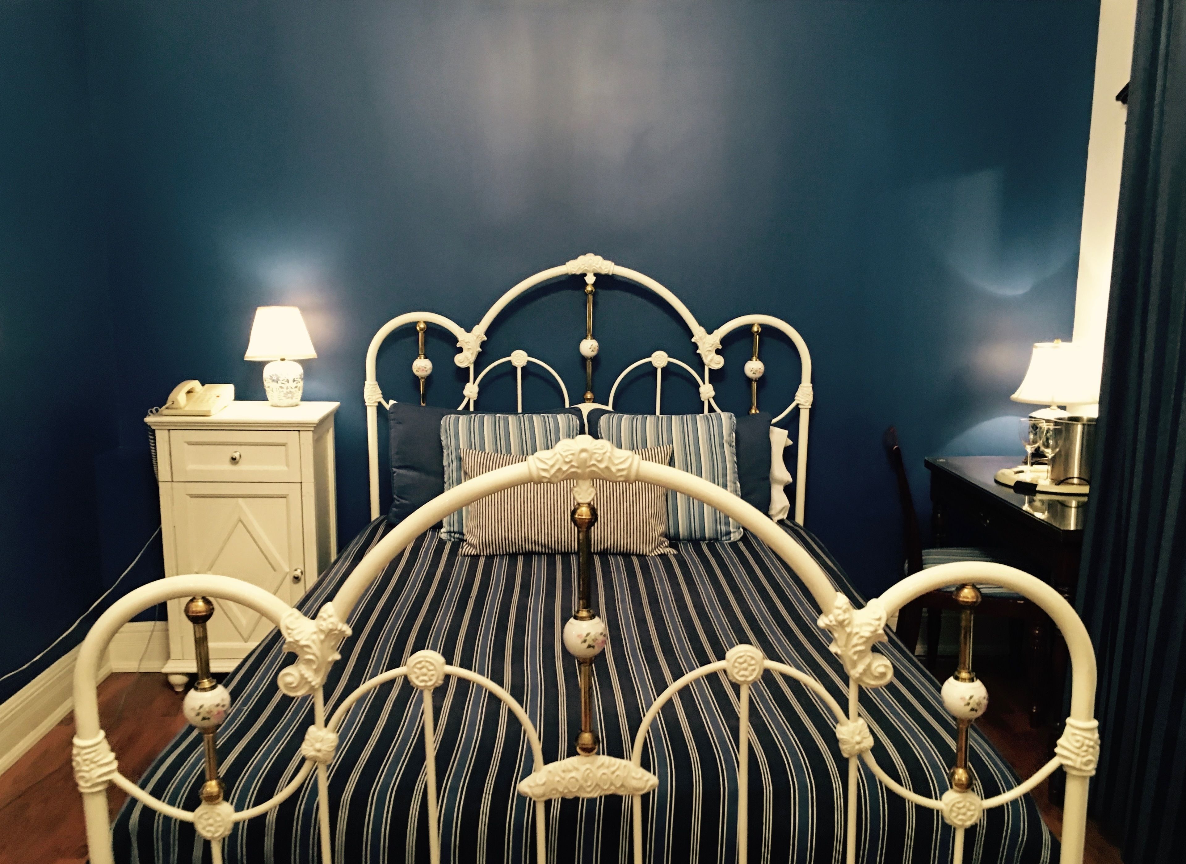Un lit avec un cadre en métal blanc et une literie à rayures, une table de chevet avec une lampe et une petite table de nuit avec une lampe.