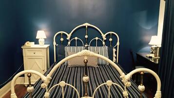 Un lit avec un cadre en métal blanc et une literie à rayures, une table de chevet avec une lampe et une petite table de nuit avec une lampe.