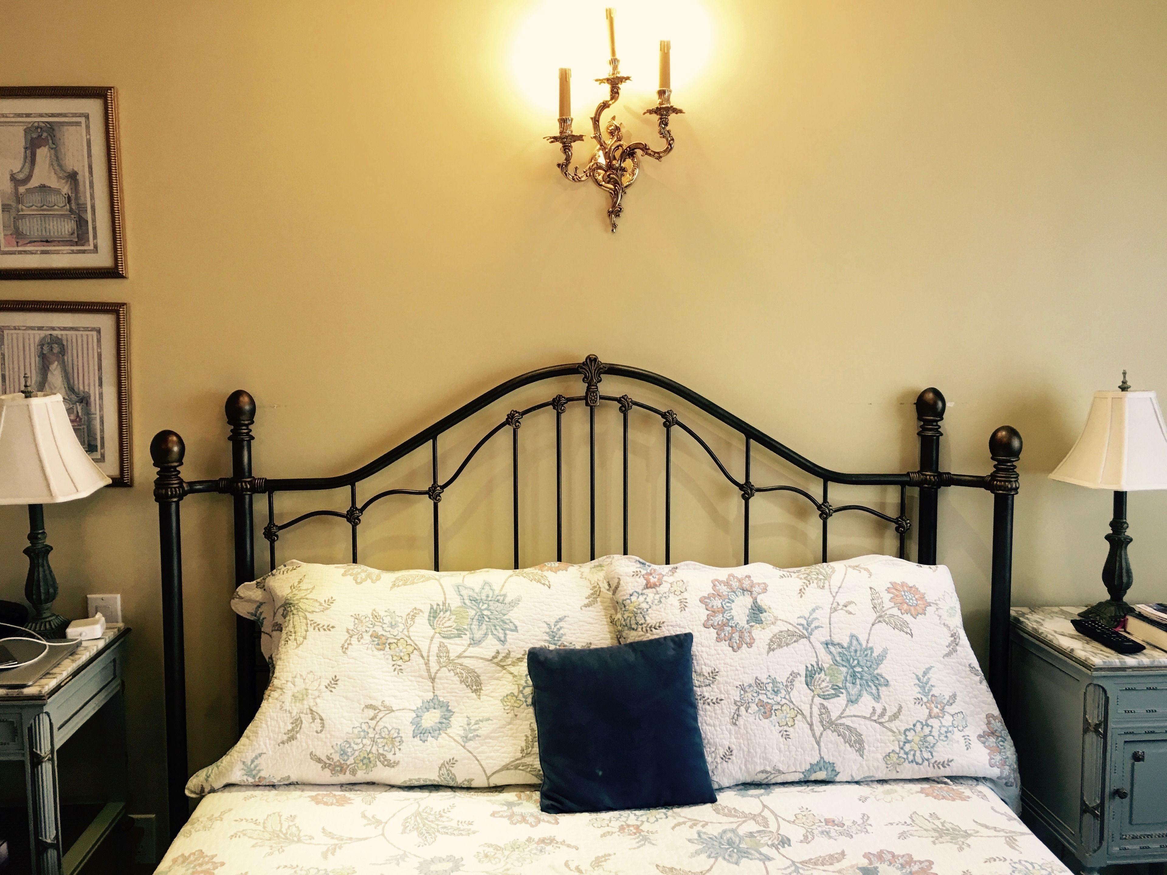 A bed with a floral bedspread, a dark blue pillow, and a wall-mounted chandelier.