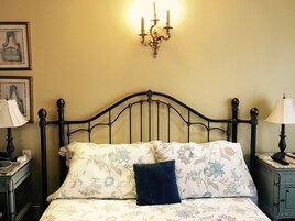 Una cama con una colcha estampada con motivos florales, un almohador azul oscuro y una araña de techo adherida a la pared.