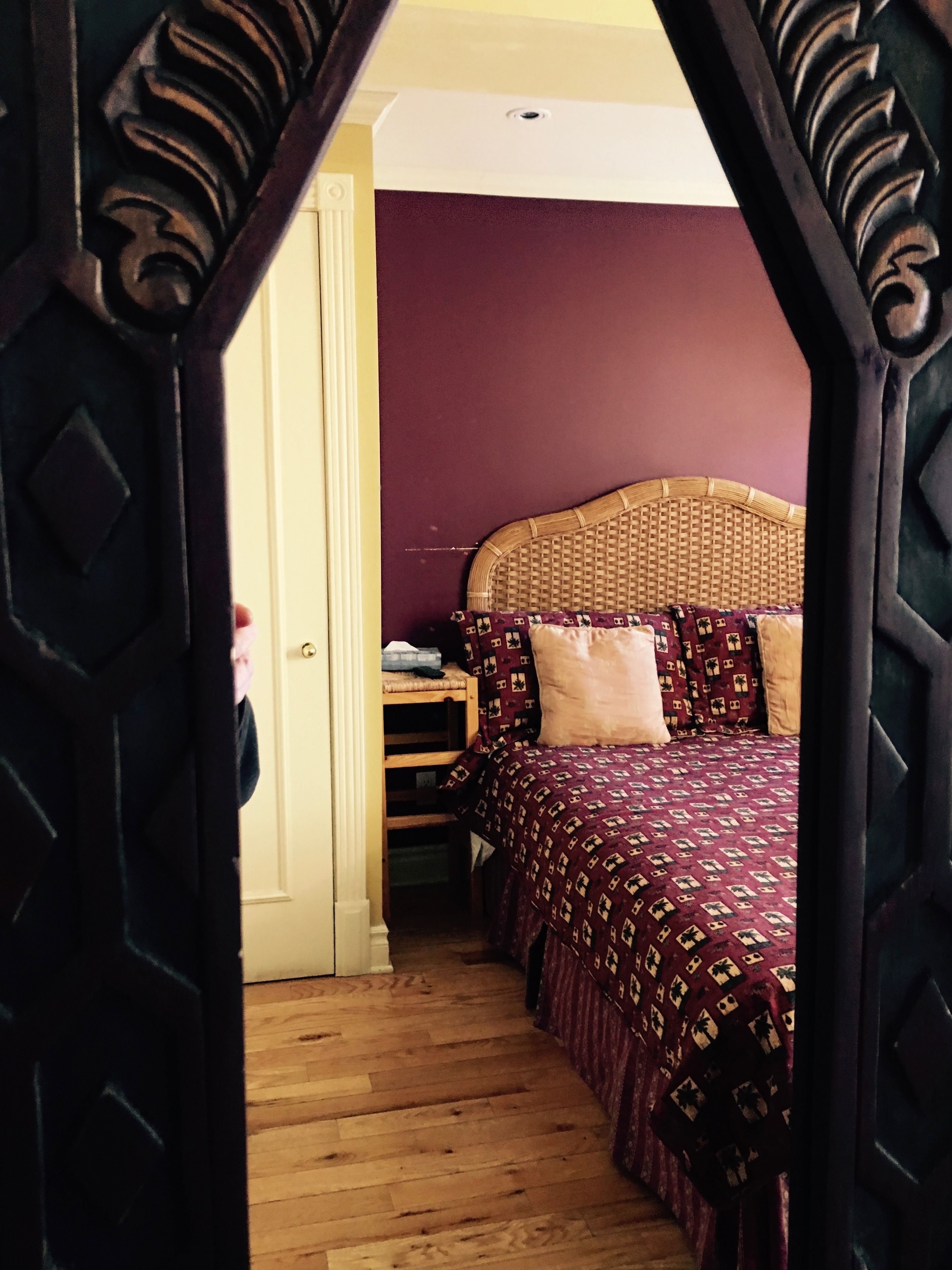 A bedroom with a wooden floor, a bed with a patterned bedspread, and a wicker headboard.