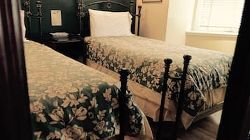 Una stanza con due letti, ognuno con una coperta a fiori e un poggiatesta in legno. C'è un comodino con una lampada e un quadro incorniciato appeso al muro.
