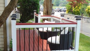 A wooden deck with outdoor furniture, a stone wall, and a view of parked vehicles. - Baywatch Hotel & Marina (Hampton Bays)
